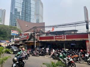 A sidestreet in Jakarta filled with motorbikes, local small cafes (warungs) and cars.