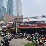 A sidestreet in Jakarta filled with motorbikes, local small cafes (warungs) and cars.